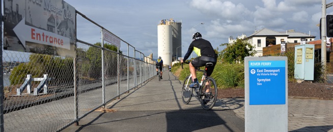 Shared path along the Mersey River in Devonport with rider in foreground turning onto path and riding in background further up the path heading towards the silo.