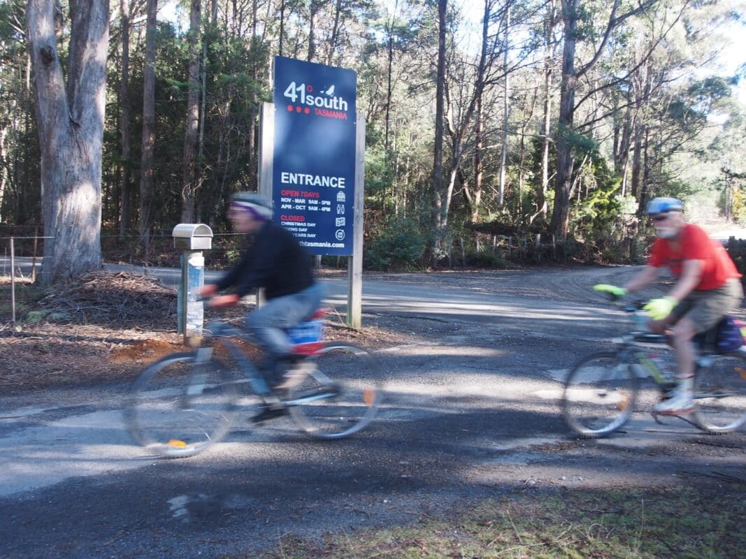 Two riders are blurred as they pass the entrance sign to 40 degree south salmon and ginseng farm outside of Deloraine.