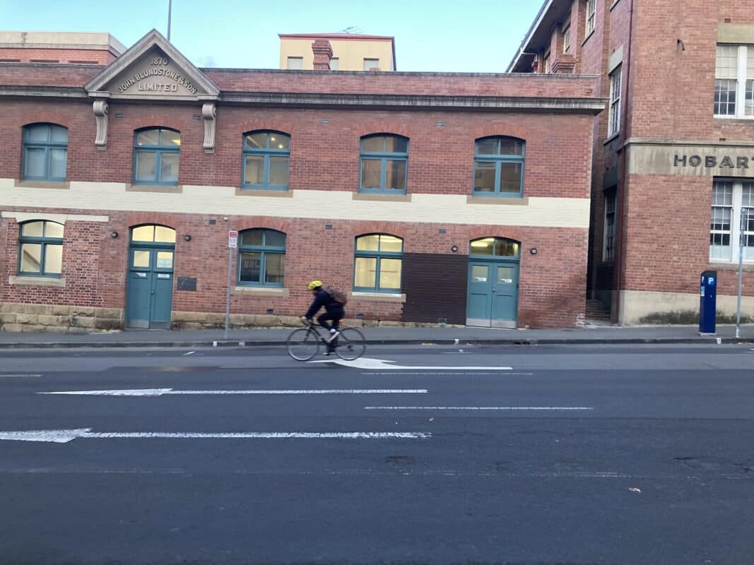 A man rides past the old Blundstone red brick factory on Campbell Street with no other users in the frame. 