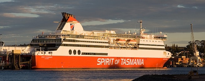 Red and white Spirit of Tasmania ferry docked with setting sun bathing it in golden light.
