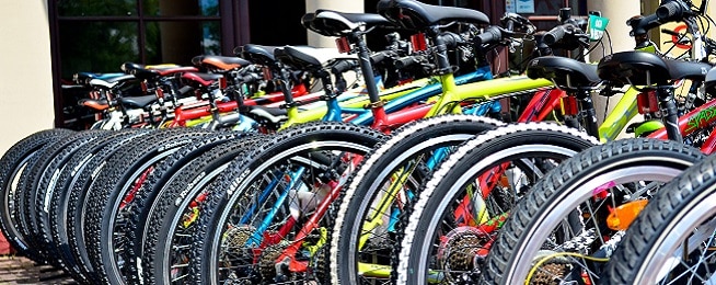 Line of colourful mountain bikes, focused on back wheel and saddles.
