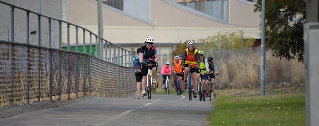 A group of women wearing a variety of colours rides along the Intercity cycleway towards the camera.