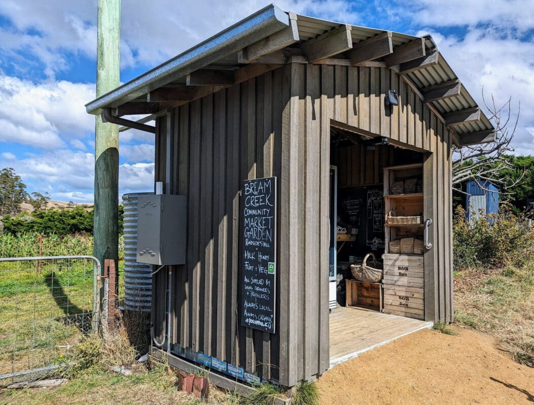Small wooden shed with blackboard sign on the side and open front showing shelving inside.