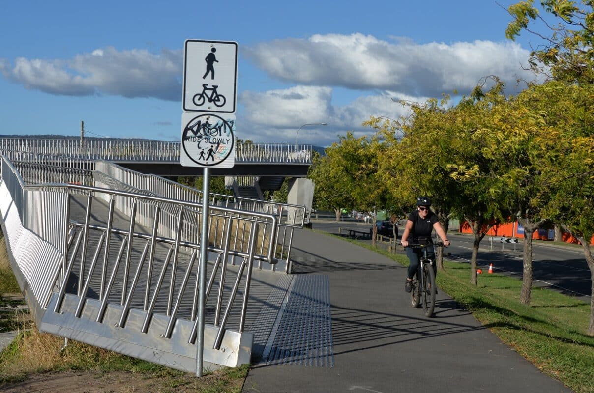 A woman in all black rides past the pedestrian bridge between the university and Launceston city centre.