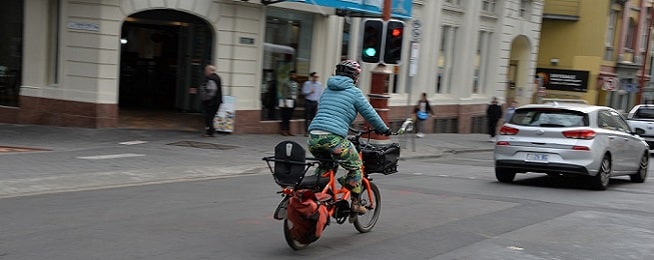 Woman rides an electric cargo bike along Collins Street in Hobart in the middle of the traffic lane.
