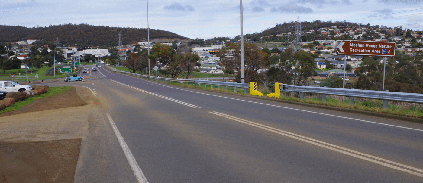 Image of road with prominent yellow opening cut into the road barrier on the right of the image.