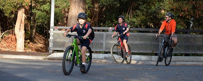 Two South Hobart Primary School students wearing uniforms ride down Anglesea Street with a parent to the school gate.