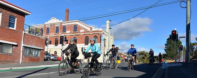 Group of people ride down Collins Street near the intersection with Molle Street with an old brick and cream building in the background.