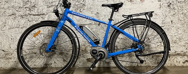 Blue e-bike with Bicycle Network branding leans against a weathered looking stone wall.