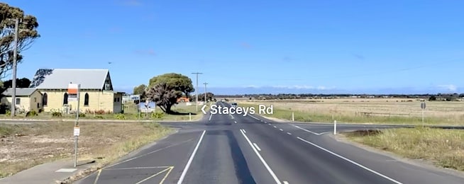 Intersection on Barwon Heads Road showing no traffic surrounded by flat grass paddocks.